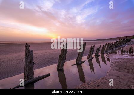 The sun setting in the distance with groynes reflecting in a rockpool Stock Photo