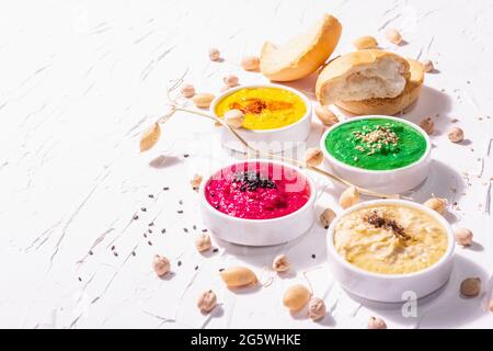 Various hummus dips, the flat lay of hummus in different colors with spinach, beetroot, turmeric and vegetables, vegan snack. White putty background, Stock Photo