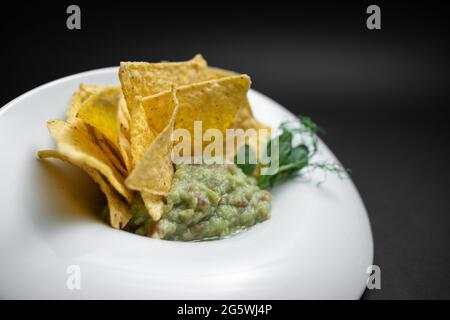 closeup of guacamole dip in bowl with avocado and nachos on black background Stock Photo