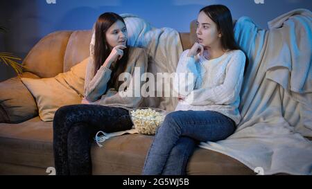 Two girls talking and discussing movie white watching TV at night Stock Photo