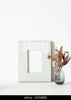 Home still life of dry autumn branches in vase and wood blue pastel frame on white table. Copy space. Front view Stock Photo