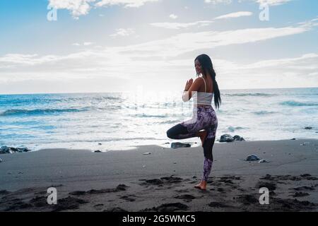 woman in sport clothes practicing yoga and meditating on beach in morning Stock Photo