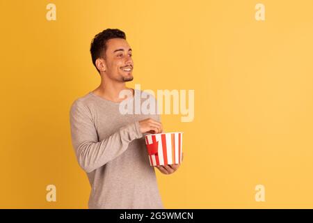 Crazy shocked, flying popcorn. Caucasian young man's portrait isolated on blue studio background. Beautiful male model in casual style. Stock Photo