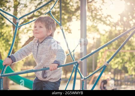 Cute smiling boy climbing rope web on a playground in South Australia on a bright sunny day Stock Photo