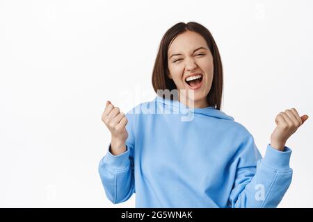 Yeah baby Im winner. Girl celebrating win, achieve success goal, shouting yes and makes fist pump gesture, triumphing, winning money prize, standing Stock Photo
