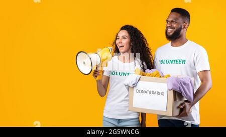 Multiethnic Volunteers Holding Donation Box Talking In Megaphone, Yellow Background Stock Photo
