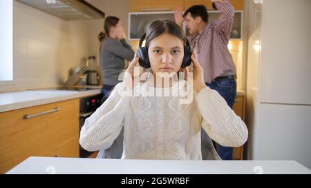 Teenage girl putting on headphones to close ears because of arguing and shouting parents. Family violence, conflicts and relationship problems Stock Photo