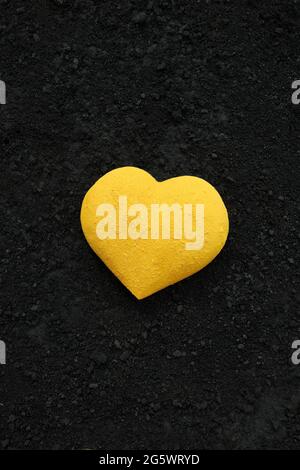 3 dimensional heart shape painted bright yellow with powder paint, placed on a background of black cinders Stock Photo