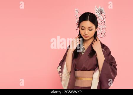 Young asian woman in kimono adjusting brunette hair isolated on pink Stock Photo