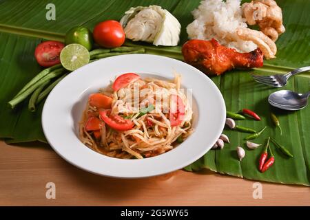 Green papaya salad or Som Tum with grilled chicken and sticky rice on wooden table. Stock Photo