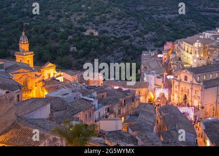 Ragusa, Sicily, Italy. View over tiled rooftops to Ragusa Ibla, dusk, façade and bell-tower of the Church of Santa Maria dell'Itria illuminated. Stock Photo