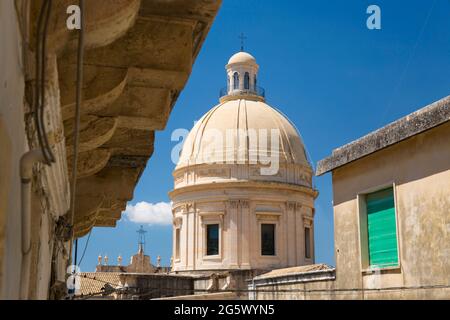 Noto, Syracuse, Sicily, Italy. View down sunlit narrow street to the reconstructed dome of the baroque Cathedral of San Nicolò. Stock Photo