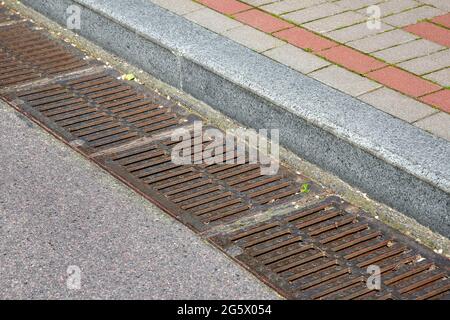rectangular hatches of the lattice of the drainage system for drainage of rainwater from the road surface with an asphalt road at the curb with a ston Stock Photo