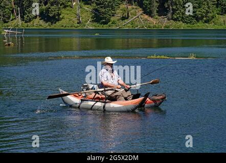 A middle-aged fisherman cooling off in a rubber raft on Clear Lake on a hot summer day in the Oregon Cascades. Stock Photo