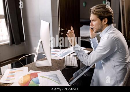 Handsome caucasian freelancer or manager talking with client making offer talking on phone near PC in home office, pensive business man making call Stock Photo
