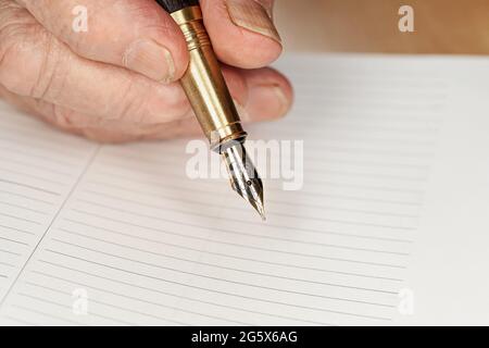 Gold coloured fountain ink pen in senior woman hand about to write something on empty daily planner page, closeup detail Stock Photo