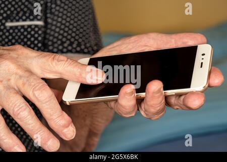 Elderly senior woman holding white mobile phone in her hands, closeup detail Stock Photo