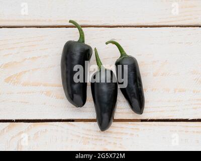 Plan view of Purple Jalapeño chilli peppers on a white wooden panelled,rustic background. Stock Photo