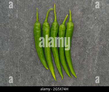Plan view of green chilli peppers on a grey textured background. Stock Photo