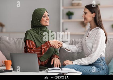 Mature Muslim Businesswoman Shaking Hands With Young Female In Office Stock Photo