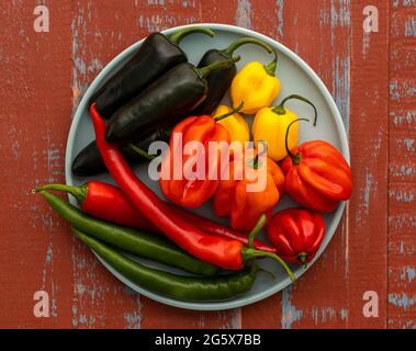 Plan view of assorted chilli peppers on a duck egg blue plate, on a brown and blue  wooden background. Stock Photo