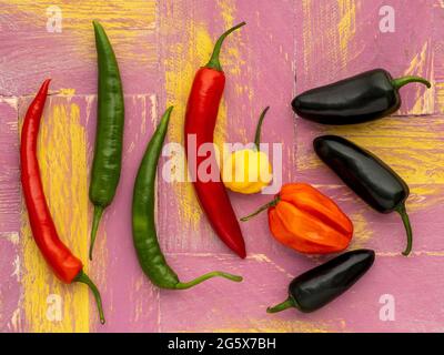 Plan view of assorted chilli peppers on a pink and yellow, wooden background. Stock Photo
