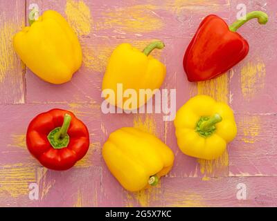 Plan view of red and yellow bell peppers on a pink and yellow  wooden background. Stock Photo