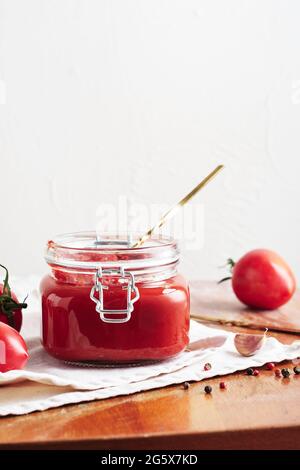 Tomato paste in a jar. Sauce, fresh tomatoes, garlic and peppers on a wooden kitchen table. Stock Photo