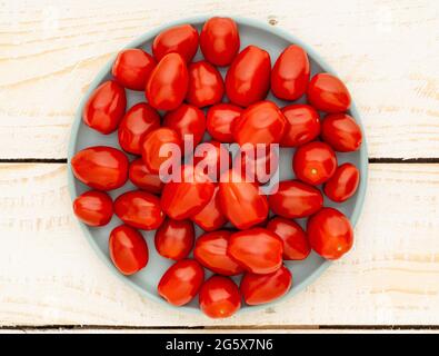 Plan view of small plum tomatoes on a duck egg blue plate, on a white wooden, rustic background Stock Photo
