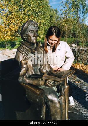 ASTRID LINDGREN statue outside the Junibacken the explore and play ground for children.Young girl  leans over the armrest and read in the book Stock Photo