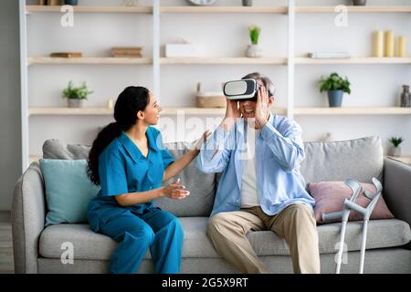 Elderly man using VR headset with young medical worker, exploring augmented reality at retirement home Stock Photo