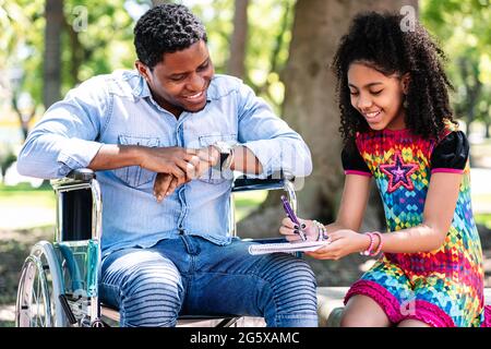 Man in a wheelchair at the park with his daughter. Stock Photo