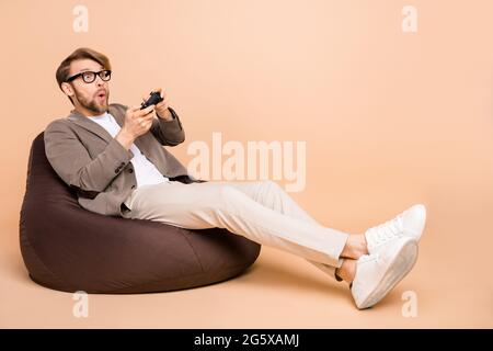 Full size photo of shocked amazed surprised man in glasses sit armchair playing playstation isolated on beige color background Stock Photo