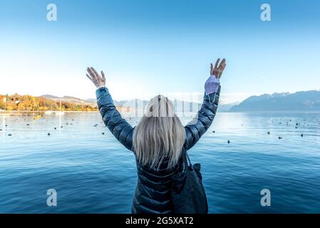 Faceless blonde woman in a lake raising her arms and holding her face mask. Stock Photo