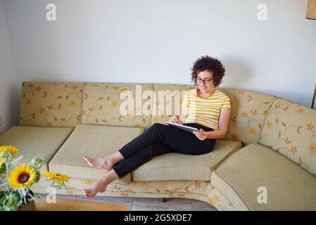 Young woman draws on her digital tablet sitting on the sofa Stock Photo