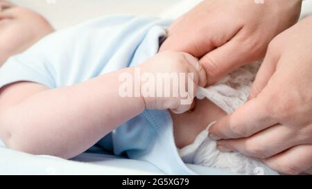 Closeup of mother taking off and changing messy diapers of her little baby lying in cradle. Concept of parent,baby hygiene and child development. Stock Photo