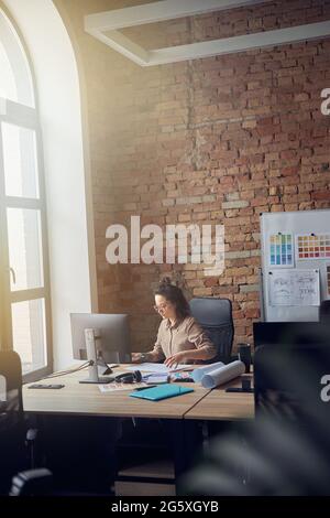 Concentrated woman in glasses, professional architect or designer working on blueprint, sitting at the table in her office Stock Photo