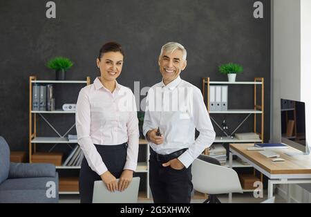 Senior male boss and young female secretary standing in office portrait Stock Photo