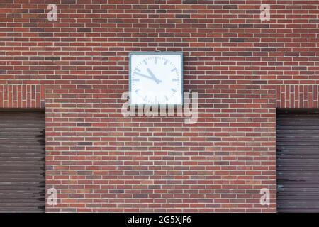 A clock hangs on a brick wall and a part of a lowered brown roller shutter is visible on the sides Stock Photo