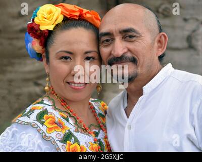 Dressed up Mexican Yucatecan couple (man and woman) with traditional hairstyles wears folkloric clothing and smiles for the camera. Stock Photo