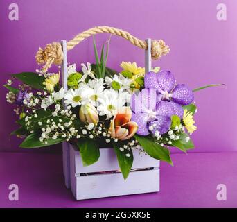 Beautiful bouquet of flowers in lilac wooden basket on purple color background. Floral visuals Floral floristic blooming composition. Stock Photo