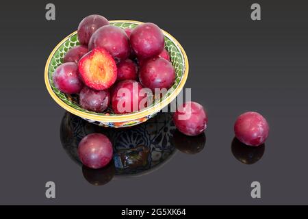 Ripe juicy plums in a bowl on black table background. Stock Photo