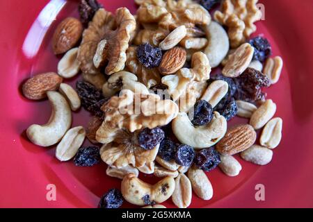 Mix of dried fruits and nuts piled up on a red bowl. Top view. horizontal. Cashew, hazelnuts, peanuts, dried apricots, viburnum, raisins Stock Photo