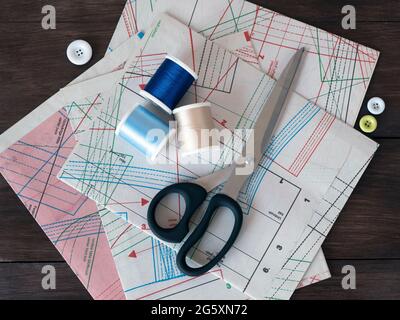 Sheets of pattern for sewing, dressmaking scissors, spools and buttons on a dark wooden background. Professional clothing patterns and sewing items Stock Photo