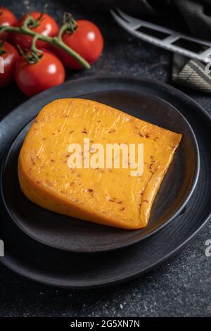 Block of hard cheese with chili flavor on plate. Stock Photo