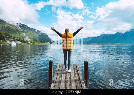 Young woman traveler with open arms standing on wooden bridge and enjoying great view on Geneva lake in Switzerland Stock Photo