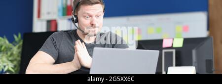 Man in wheelchair and wearing headphones with microphone works on laptop Stock Photo