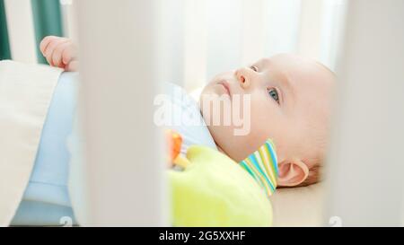 View through banister on little baby playing with toy in cradle. Concept of parenting, family happiness and baby development Stock Photo