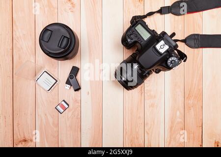 Seen from above, on some light-colored wooden boards there is a digital camera, a lens, two memory cards and a flash drive. Stock Photo
