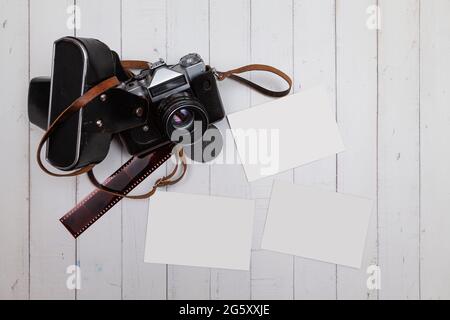 Seen from above, on white wooden boards there is an analog camera, a strip of negatives and three blank photos to customize as a mockup. Stock Photo